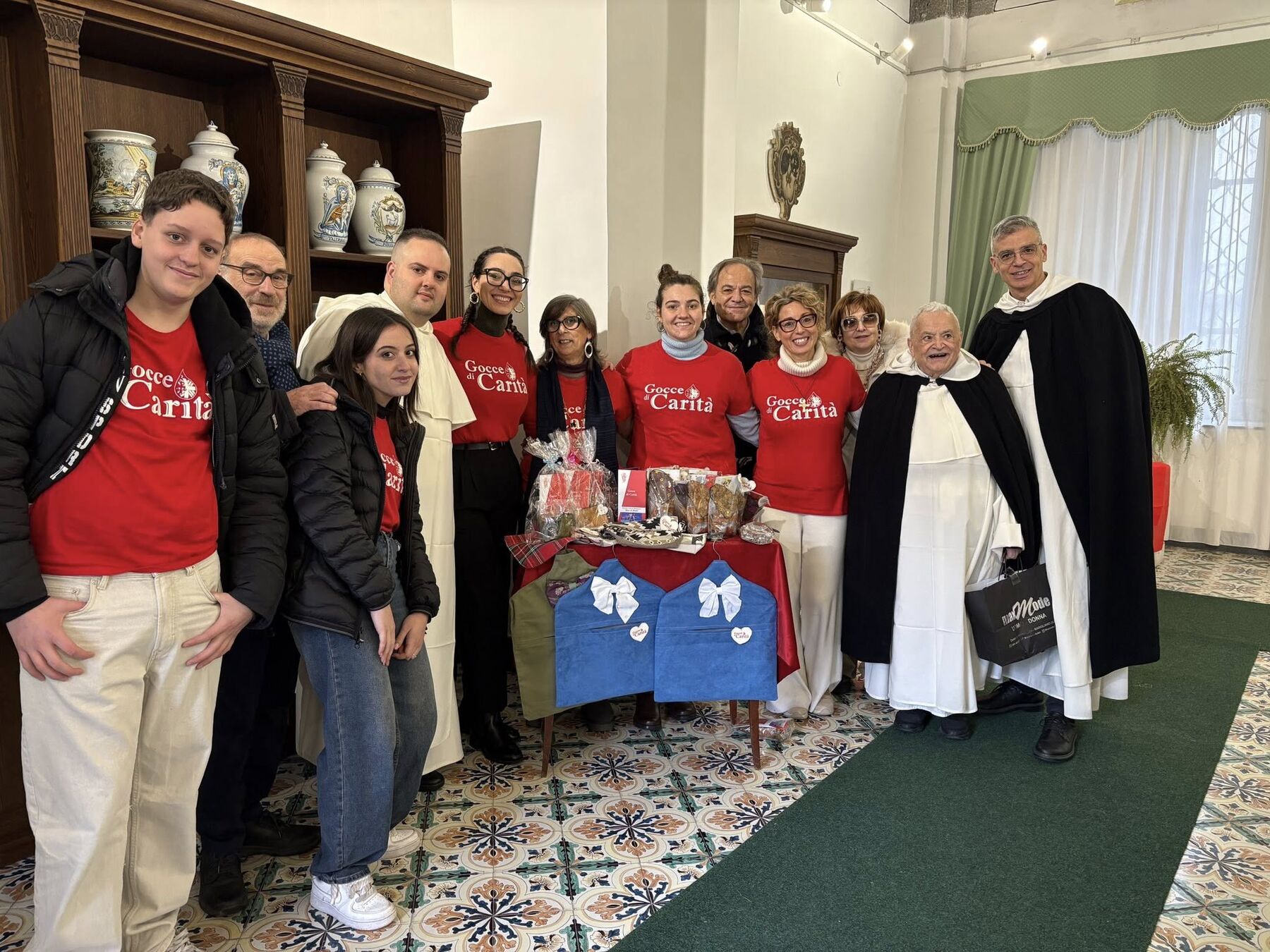 I volontari di Gocce di Carità con le magliette rosse insieme ai religiosi, davanti agli antichi vasi da farmacia